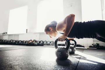 Slim brunette doing push-ups exercises on kettlebells. Cross fit training. focus on kettlebells