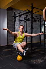 Cross fit fitness man standing on one leg and balance on the kettlebells in the gym against brick wall.