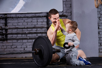 Portrait of happy father and son with barbell in the cross fit gym against brick wall.