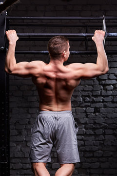 Rear view photo of muscular male doing exercises on horizontal bar against brick wall at the cross fit gym.