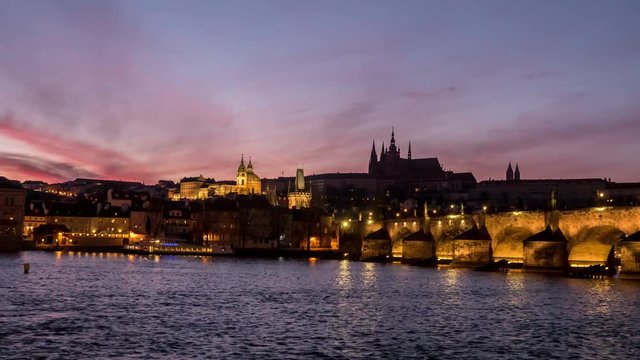 Splendid view on the Charles Bridge with anamazing dark red and grey skyscape. streaming ships, sparkling waters of the Vltava river n the evening twilights, taken as a timelapse and zoom out shot