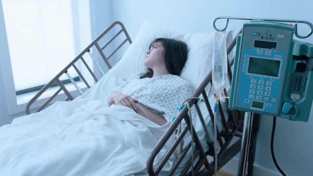 A sick young woman with an IV recovering in a hospital bed next to a window, slow motion, 4K