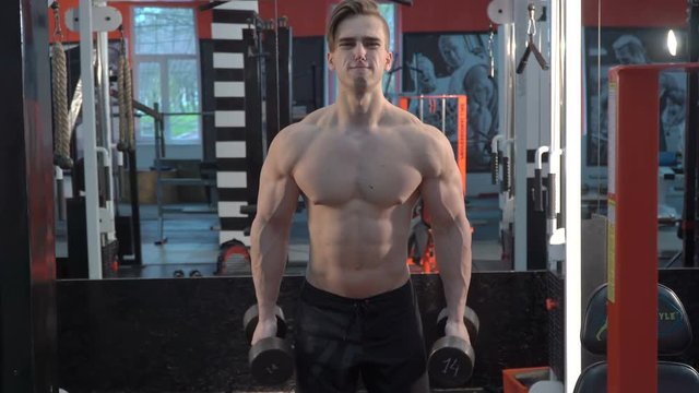 Muscular bodybuilder guy doing exercises on biceps with dumbbells in gym