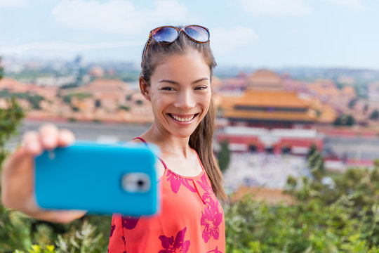 china travel. Young Asian woman tourist taking selfie pictures with mobile phone with background landscape view of the forbidden City in Beijing. Asia summer destination.