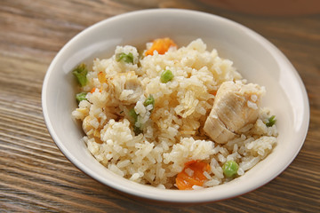 Delicious rice with chicken and vegetables in plate on wooden table