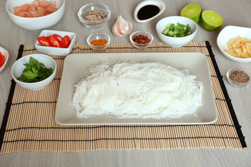 Plate with rice noodles and ingredients on wooden table