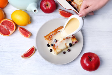 Pouring sauce on tasty bread pudding with berries on table