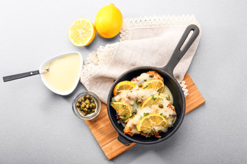 Frying pan with delicious chicken piccata on wooden board