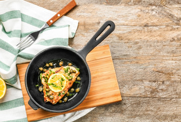 Frying pan with delicious chicken piccata on wooden board