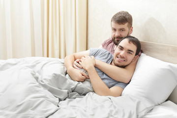 Fototapeta premium Happy gay couple hugging in bed at home