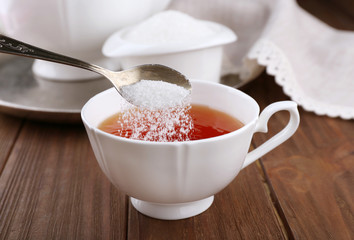 Adding sugar to cup of black tea on wooden table