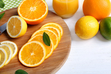 Wooden board with sliced citrus fruits on light background