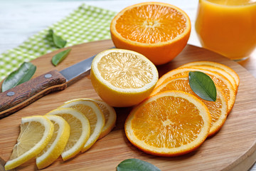 Wooden board with sliced citrus fruits on light background