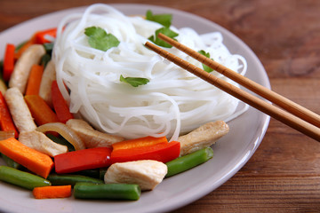 Plate with tasty rice noodle and vegetables on wooden table
