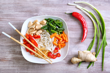 Plate with tasty rice noodle and vegetables on wooden table
