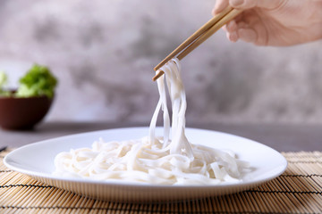 Human hand taking rice noodle from white plate