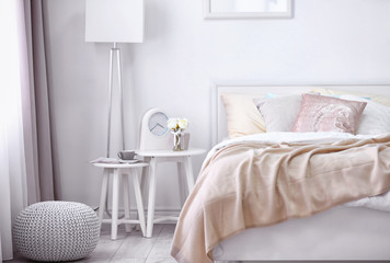 Comfortable bed with soft beige coverlet and pillows in light modern room