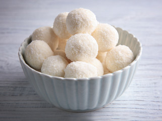 Bowl with tasty candies in coconut flakes on wooden table
