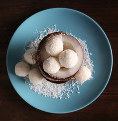 Plate with tasty candies in coconut flakes and fresh nut on wooden background