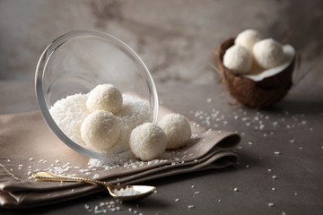 Bowl and tasty candies in coconut flakes on gray table