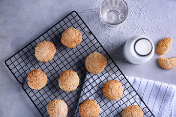 Baking rack with tasty coconut cookies and bottle of milk on table