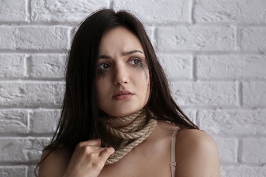 Woman with rope around neck on brick wall background
