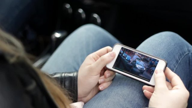 Teenager watches generic show on smartphone in car of rainy downtown city
