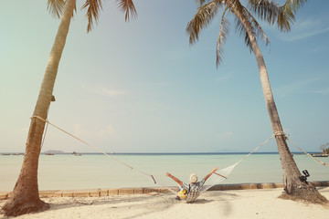 Photo taken on Phi Phi Don island in Krabi province, Thailand. A man enjoys a holiday on a tropical island. He lies on a hammock stretched between two tall palms.
