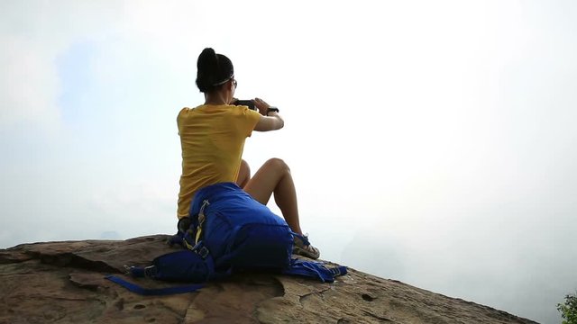 Young woman hiker taking picture with smartphone on mountain peak