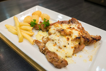 Pork steak with cheese served with french fries and hash brown potato on white plate.