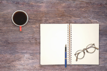 A cup of coffee, book,pen and eyeglasses on wood table,top view.