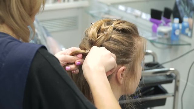 Portrait of a young woman in a beauty salon: creating a magnificent setting from curls. A blonde in a hairdresser does a beautiful hairstyle. Hair care and creating an image.
