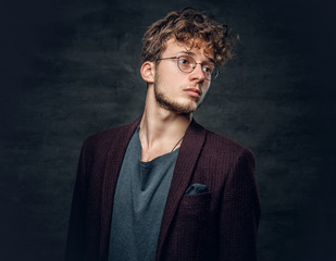 A man with curly hair dressed in a jacket and eyeglasses.