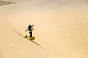 Man with a backpack runs on hot yellow sand in the desert