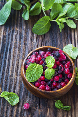 Fresh frozen fruits with mint leaves in wooden bowl