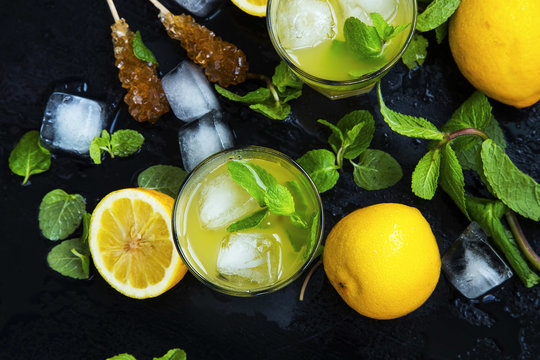 Top view of lemon and mint drinks with ice and sugar sticks on dark background