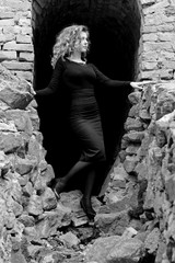 Beautiful sexy and elegant thin young light blonde european woman in total black dress and heels around old ruins in vintage style have a secret in her soul and finding the answer