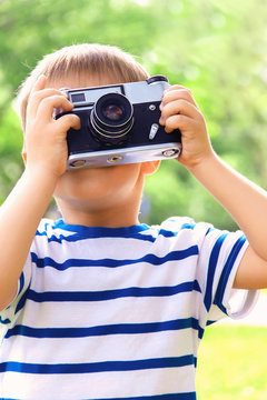 Happy cheerful boy with a camera, the baby photographed outdoors, soft focus