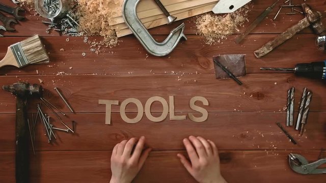 Top view time-lapse of a hand laying on wodden table word "TOOLS"