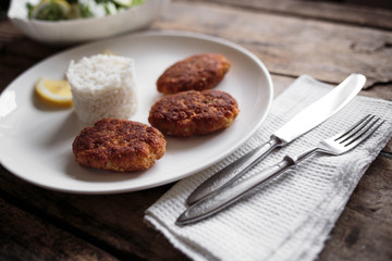 Three croquettes on white ceramic plate with cutlery aside on wooden table