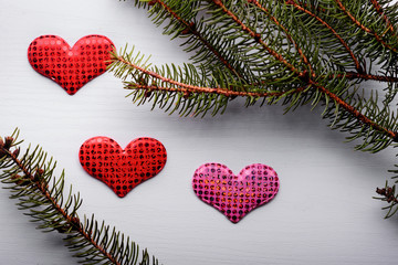 Wooden white background with a branch of pine and three hearts.