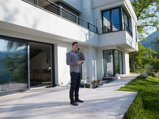 man using mobile phone in front of his luxury home villa