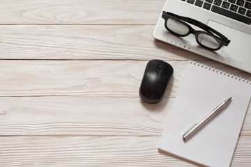 Workplace. Laptop, black glasses, pen, notebook, black mouse on the white wooden background.