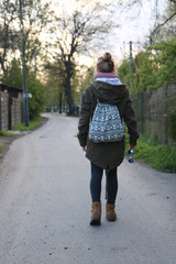 Samotna dziewczyna idzie drogą wiejską, na plecach ma mały plecak, w ręce okulary słoneczne, odwrócona jest tyłemc © Wioletta