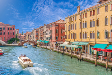 Venice Grand canal with gondolas, boats, bridge, and colorful houses. Italy in summer bright day with blue sky and white clouds