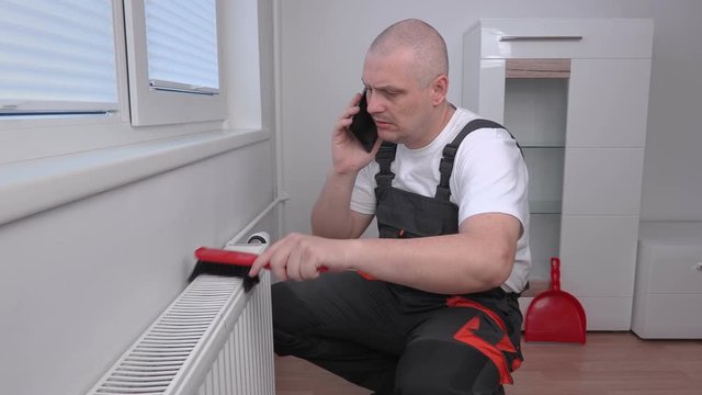 Plumber cleaning radiator and talking on phone