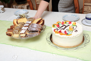 Tort urodzinowy i ciasta na stole podaje kobieta na tacy.
