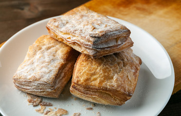 Puff pastry cookies in a white plate on a wooden table, selective focus, closeup shot