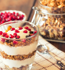 yogurt with homemade granola and pomegranate on the bright wooden board..