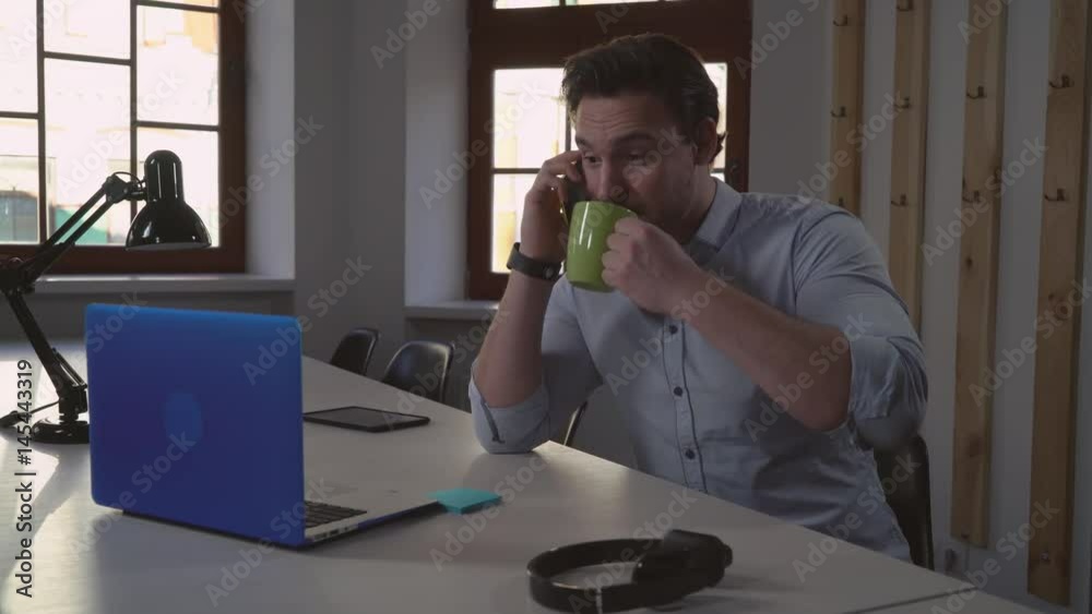 Poster adult man using smartphone in the office. handsome geek sitting at the desk with laptop has conversa